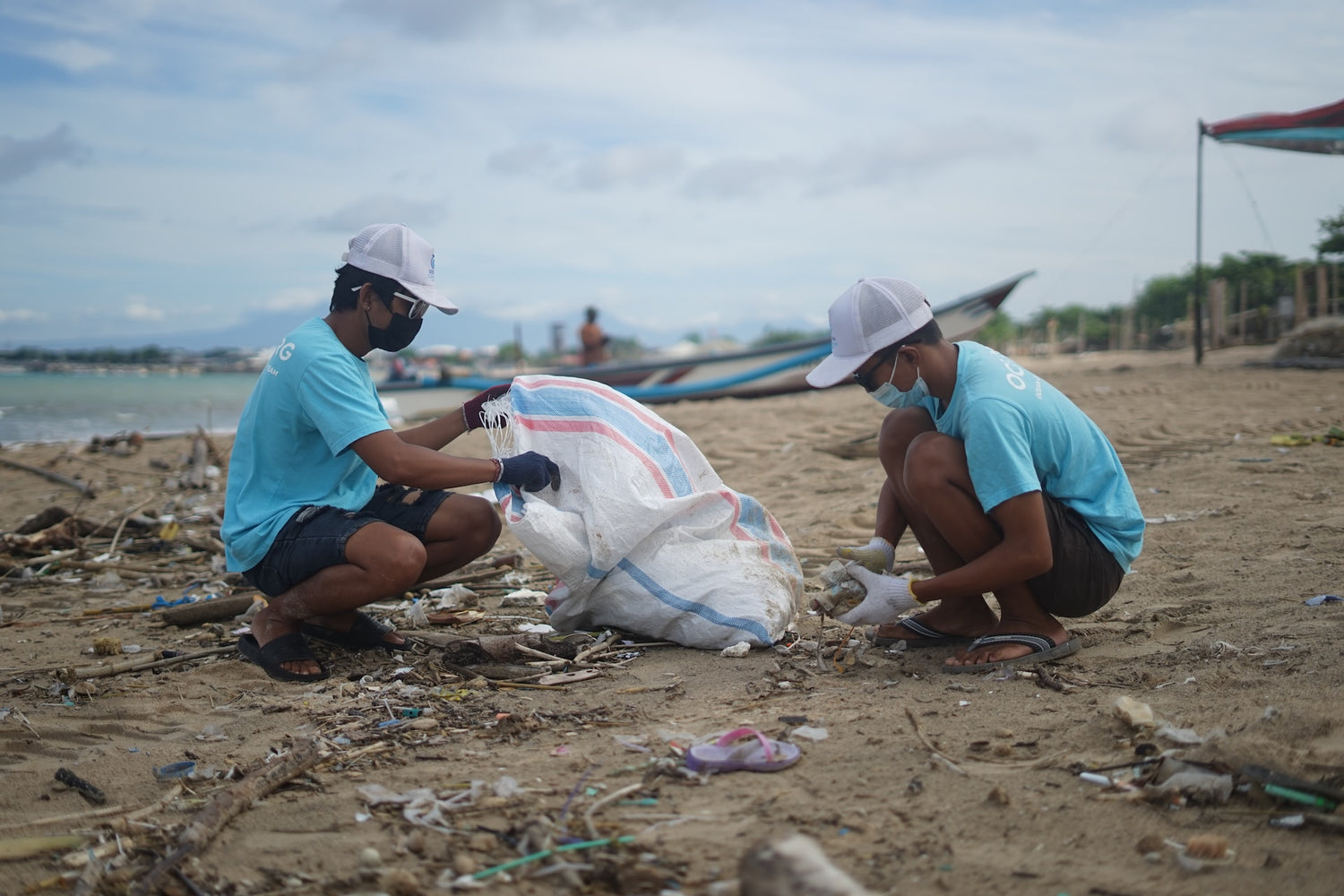 Two men in blue shirts recycling plastic waste on a beach in Asia